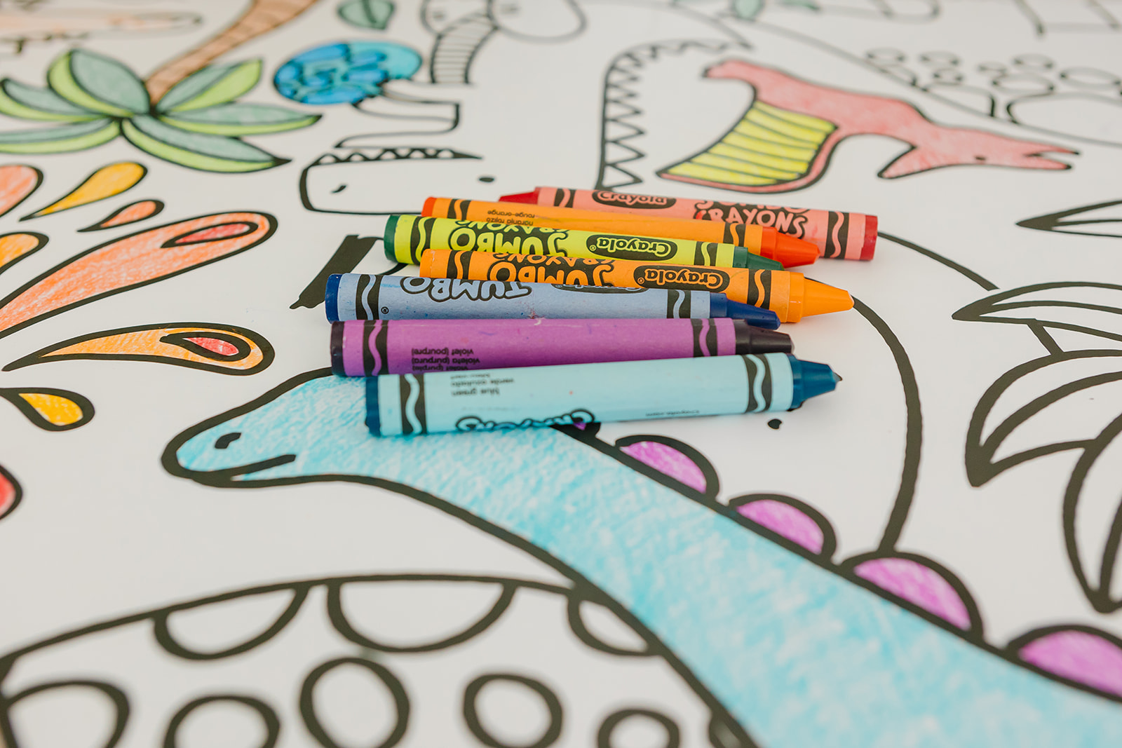 Colorful crayons resting on a dinosaur coloring banner