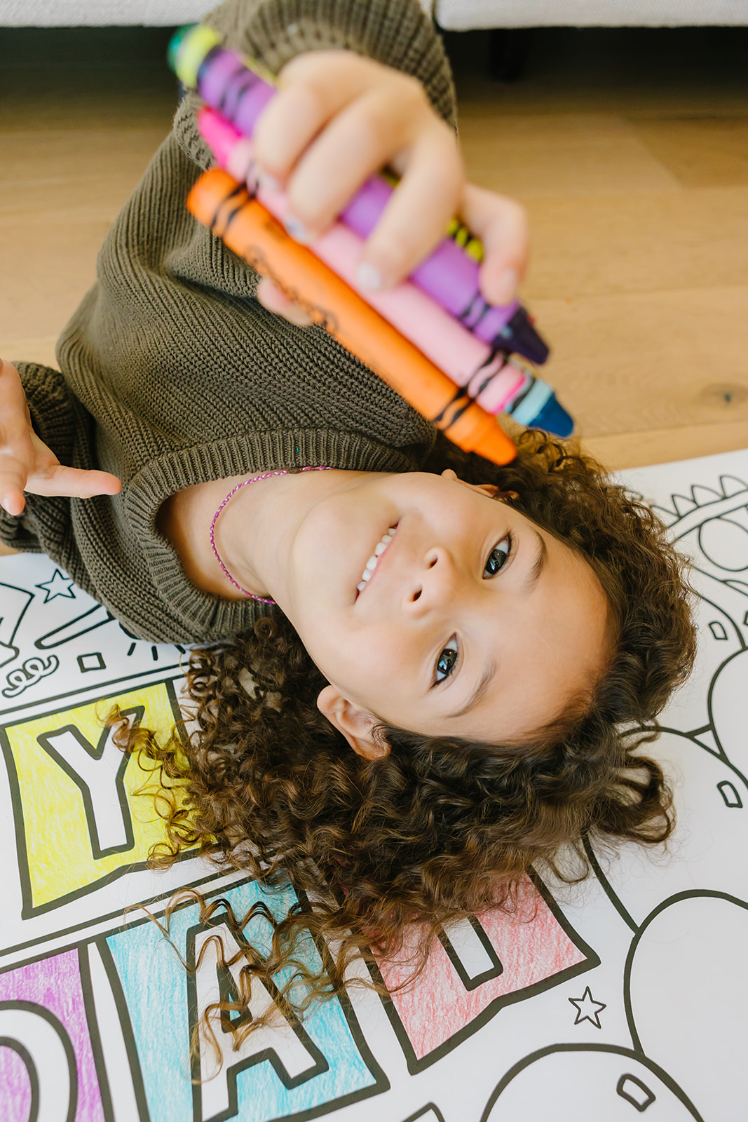 Happy girl holding colorful crayons while lying on a giant coloring banner
